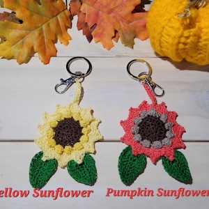 May include: Two crocheted sunflower keychains, one yellow and one orange, with green leaves. The yellow sunflower keychain is labeled "Yellow Sunflower" and the orange sunflower keychain is labeled "Pumpkin Sunflower".