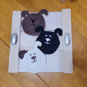 May include: Three crocheted dog-shaped coasters. One is brown, one is black, and one is white.