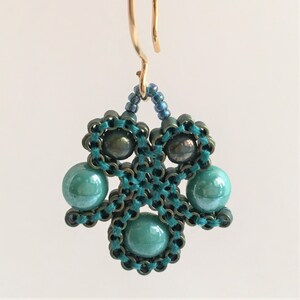 May include: Teal green beaded earrings with a gold hook. The earrings are made with small beads and larger round beads.
