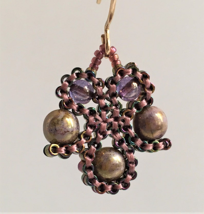 K&ouml;nnte beinhalten: Ein Paar Ohrringe in Lila und Gold. Die Ohrringe sind aus kleinen Perlen gefertigt und haben ein baumelndes Design.