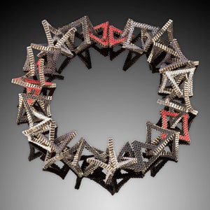 Könnte beinhalten: Eine runde Halskette aus kleinen, miteinander verbundenen Metalldreiecken. Die Dreiecke sind in den Farben Schwarz, Silber und Rot gehalten.