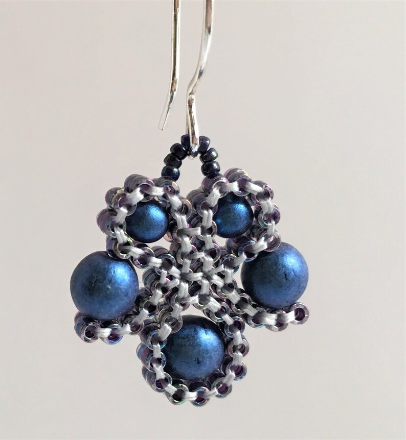 K&ouml;nnte beinhalten: Ein Paar silberne Ohrringe mit einem blauen Perlenmuster. Die Ohrringe sind aus kleinen, runden Perlen in dunkelblauer Farbe gefertigt. Die Perlen sind in einem geometrischen Muster angeordnet, was einen einzigartigen und stilvollen Look erzeugt.