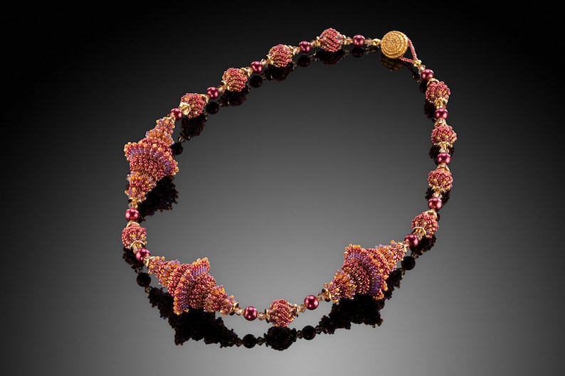 Pu&ograve; includere: Una collana di perline color borgogna e oro con un design unico che presenta pi&ugrave; piccole perline a forma di cono.
