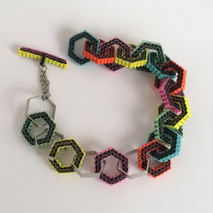 May include: A colourful bracelet made of linked hexagons with black trim. The bracelet has a silver clasp and chain.