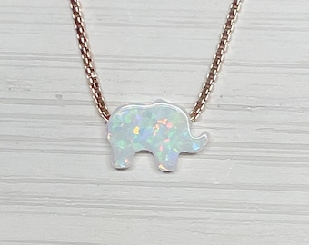 May include: A delicate silver chain necklace with a small white opal elephant pendant. The opal has a rainbow iridescent sheen.