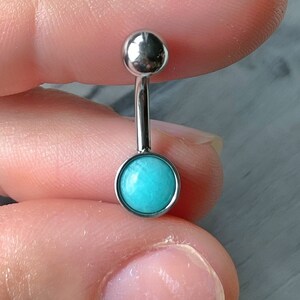 May include: A silver belly button ring with a turquoise gem. The ring is made of surgical steel and is suitable for body piercing.