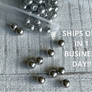 May include: A bag of silver metal balls, with some scattered on a white wooden surface. The text "SHIPS OUT IN 1 BUSINESS DAY!" is visible in the image.