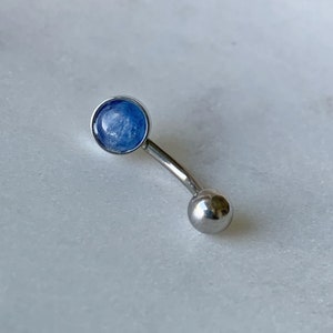 May include: A silver belly button ring with a blue gemstone. The ring is curved and has a small ball on the end.