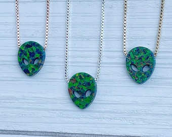May include: Three silver chains with green and blue alien head pendants. The chains are on a white wooden background.