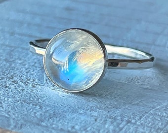 May include: A silver ring with a round, iridescent moonstone set in the center.