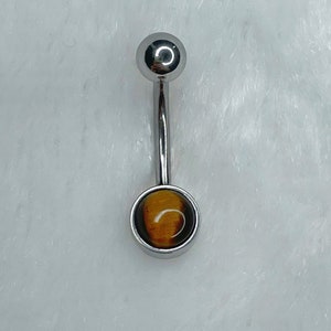 May include: A silver belly button ring with a round, brown and gold tiger's eye gemstone.