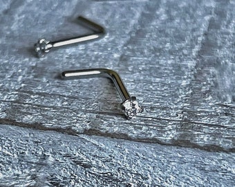 May include: Two silver nose rings with a clear gemstone on the end. The rings are bent at a 90-degree angle.