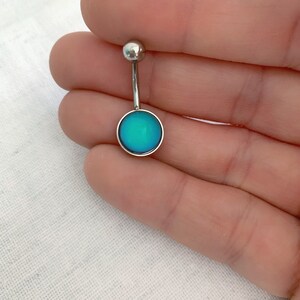 May include: A silver belly button ring with a round, blue gem. The gem has a slight iridescent quality.