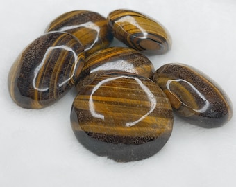 May include: Six smooth, polished tiger's eye stones in various shades of brown and gold. The stones are oval shaped and have a glossy finish.