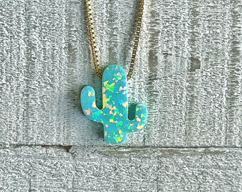 May include: A gold chain necklace with a light blue opal cactus pendant. The pendant has a sparkly, iridescent finish.