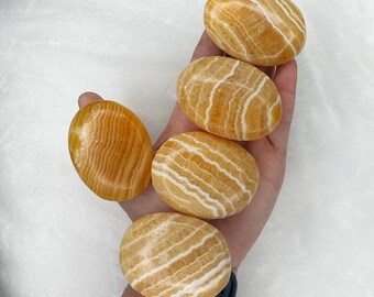 May include: Five smooth, oval-shaped stones with a yellow and white striped pattern. The stones are arranged in a hand, with the largest stone at the top.