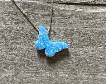 May include: A silver chain necklace with a blue opal butterfly pendant. The butterfly is iridescent and has a sparkly finish.