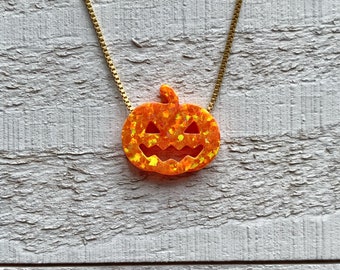 May include: A gold chain necklace with an orange glitter pumpkin pendant. The pumpkin has a carved jack-o'-lantern face.