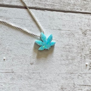 May include: A silver chain necklace with a blue opal marijuana leaf pendant.