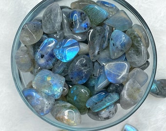 May include: A bowl filled with tumbled labradorite stones. The stones are a mix of blue, gray, and green with iridescent flashes.
