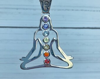 May include: Silver necklace with a pendant shaped like a person in a yoga pose. The pendant has seven colorful gemstones representing the seven chakras.