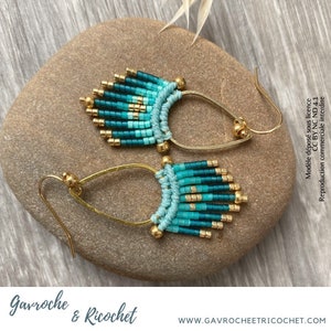 May include: A pair of turquoise and gold beaded earrings with a teardrop shape. The earrings are hanging from a gold hook.
