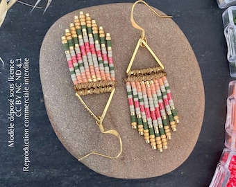 May include: Handmade beaded earrings with gold-colored metal accents. The earrings feature a geometric design with a mix of green, pink, and gray beads. The earrings are displayed on a stone surface. The brand name "Gavroche & Ricochet" is visible.
