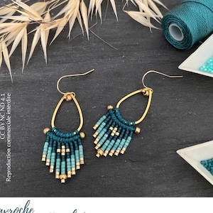 Könnte beinhalten: Ein Paar goldene Creolen mit türkisfarbenen und blauen Perlenfransen. Die Ohrringe liegen auf einer dunklen Oberfläche mit einer Spule türkisfarbenen Fadens und einer kleinen Schale mit türkisfarbenen und blauen Perlen.