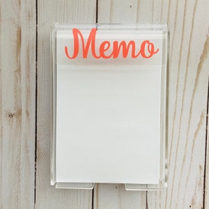 May include: A clear acrylic memo holder with a white notepad and the word "Memo" in orange lettering.