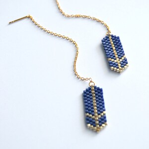 May include: A pair of gold chain earrings with blue and gold beaded pendants. The pendants are rectangular and have a geometric design.