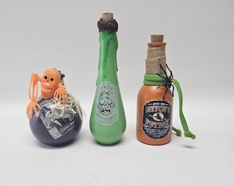 May include: Three Halloween-themed bottles. A dark blue orb with a skeleton, a green bottle labeled "Zombie Antivirus", and an orange bottle labeled "Witch Potion" with a spider.