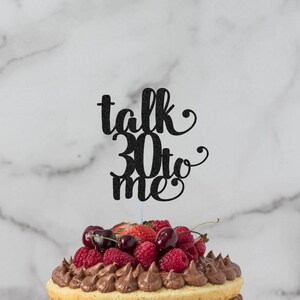 May include: A three-tiered cake decorated with chocolate frosting and fresh berries. The cake is topped with a black glitter cake topper that says "talk 30 to me".