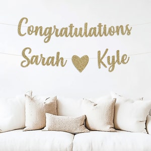 May include: Gold glitter banner with the text "Congratulations Sarah Kyle" and a gold glitter heart between the names.