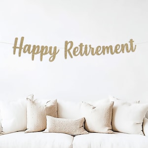 May include: A gold glitter banner with the text "Happy Retirement" hanging on a white wall above a white couch with beige throw pillows.