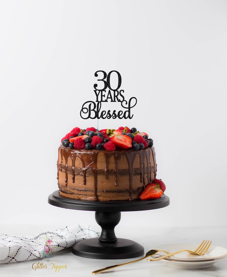 May include: A chocolate cake with chocolate ganache and fresh berries topped with a black glitter cake topper that reads "30 Years Blessed".