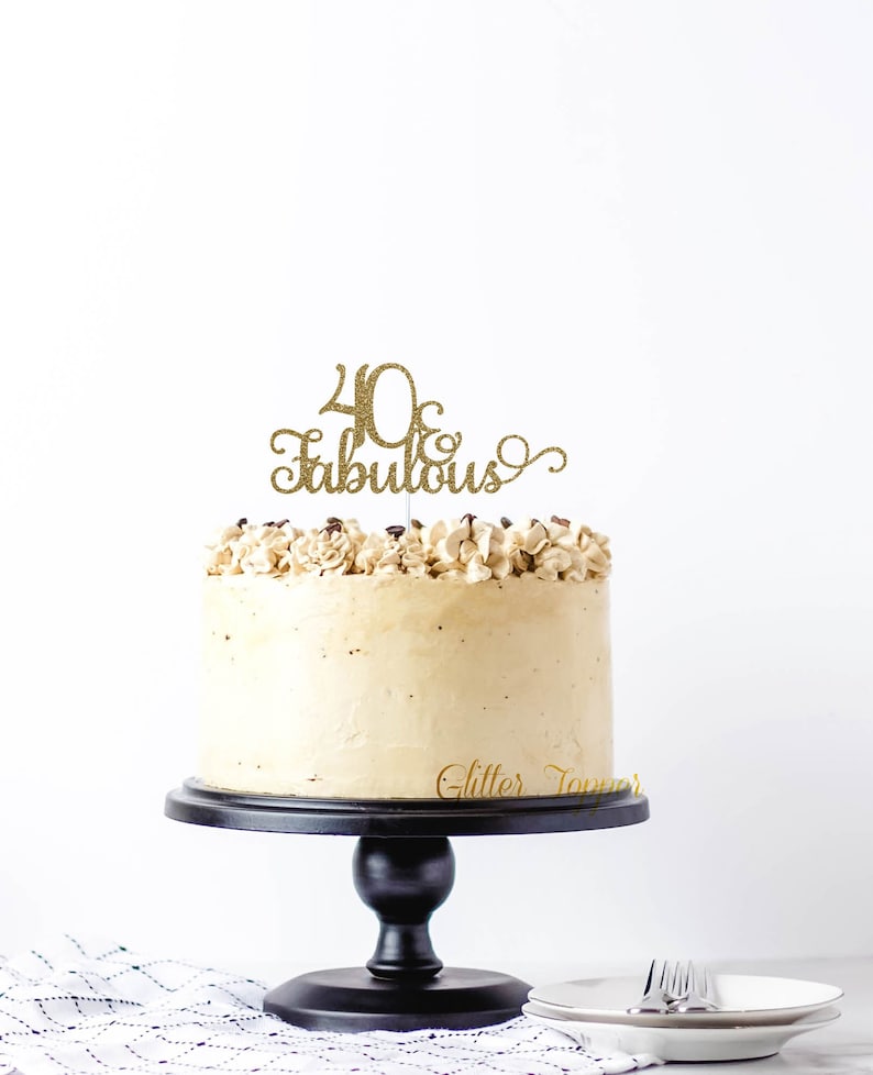 May include: Gold glitter cake topper with the text "40 & Fabulous" on a beige frosted cake.