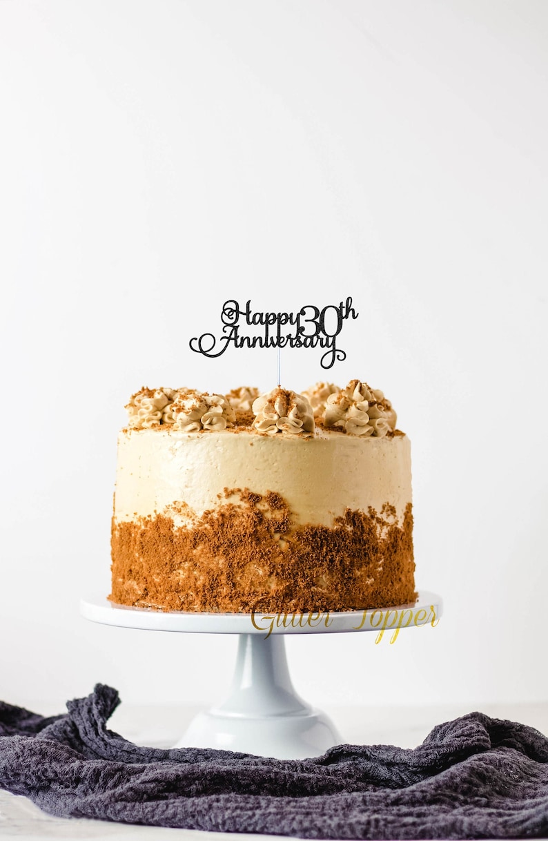 May include: A cake decorated with a brown crumb crust and a black cake topper that says "Happy 30th Anniversary".