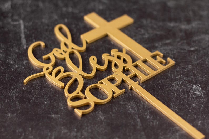 Pu&ograve; includere: Un topper per torta color oro caratterizzato da una forma a croce integrata con il testo God Bless SOPHIE in una combinazione di caratteri corsivi e stampatello. Il topper include un lungo e sottile picchetto verticale per l'inserimento nel dolce.