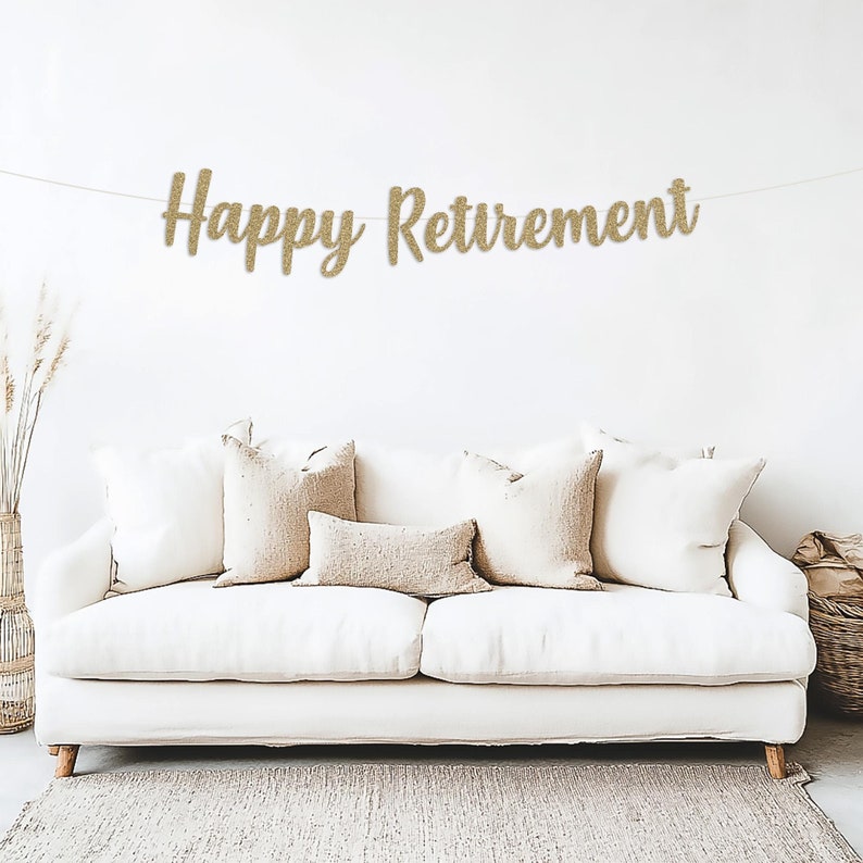 May include: A gold glitter banner with the text "Happy Retirement" hanging on a white wall above a white couch with beige throw pillows.