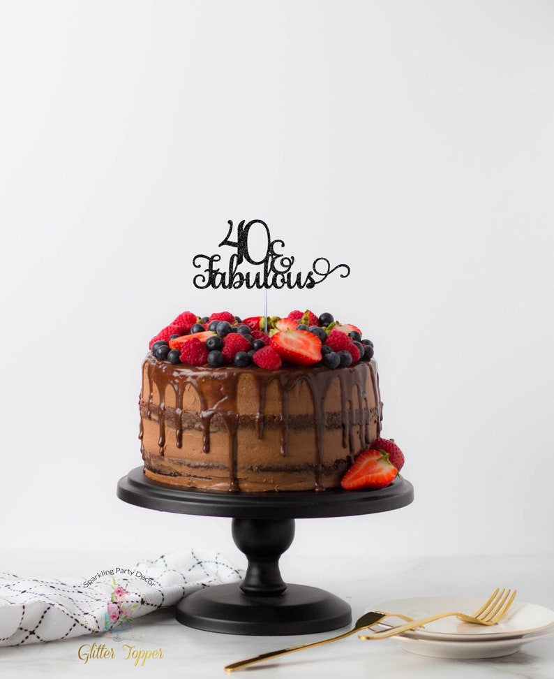 May include: A two-tier chocolate cake decorated with fresh berries and a black glitter cake topper that says "40 & Fabulous". The cake is on a black cake stand.