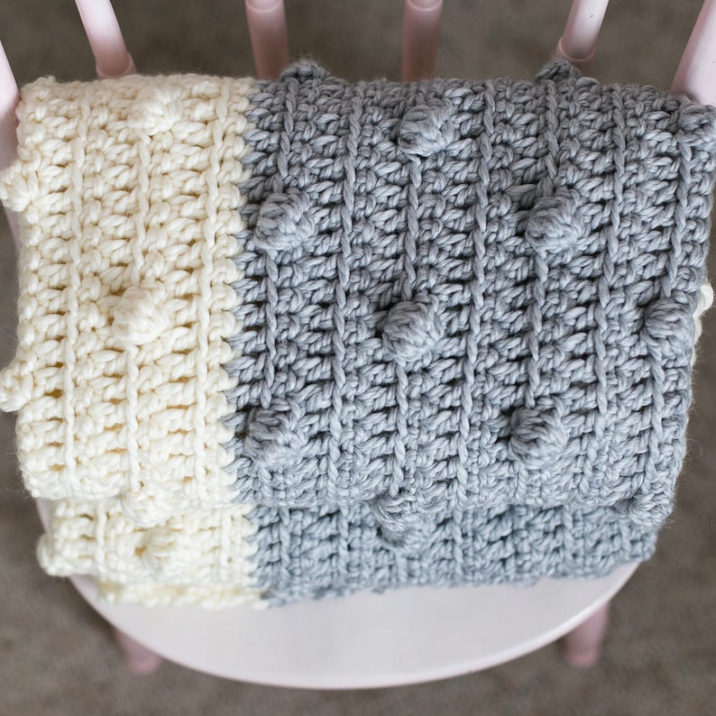 May include: A crocheted baby blanket in white and grey with a textured pattern featuring raised bumps.