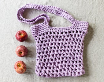 May include: A purple crocheted mesh bag with three red apples on a light gray linen background.
