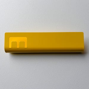 May include: A rectangular, mustard yellow power bank with a smooth, matte finish. The device features a prominent, stylized letter E logo embossed on the left side, which is slightly lighter in color than the rest of the casing.