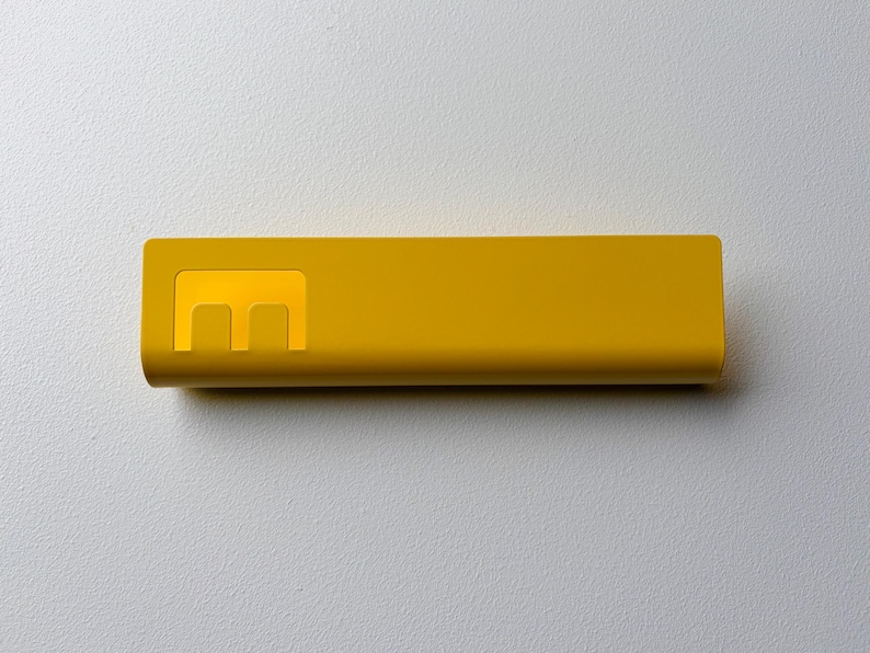 May include: A rectangular, mustard yellow power bank with a smooth, matte finish. The device features a prominent, stylized letter E logo embossed on the left side, which is slightly lighter in color than the rest of the casing.