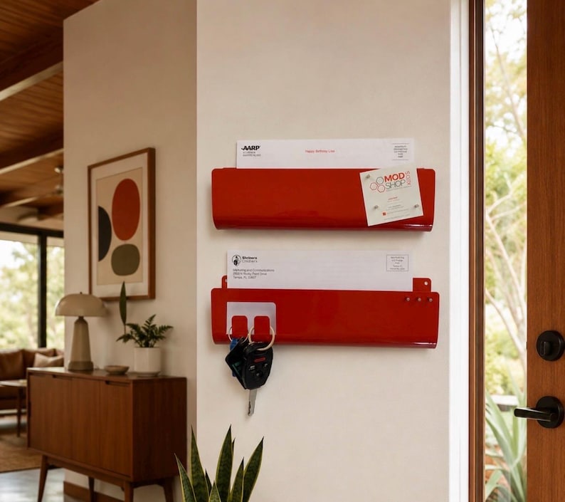 May include: Two glossy red metal wall-mounted mail organizers stacked vertically. The top organizer holds a white envelope with AARP text and a Mod Shop card. The bottom organizer holds a white envelope and has a key ring with black keys attached.