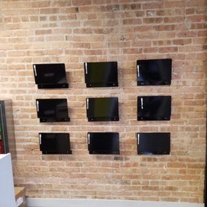 May include: Nine black rectangular frames are mounted on a brick wall. The frames are evenly spaced in three rows of three.