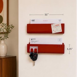 May include: Two red metal wall-mounted mail organizers with a glossy finish. Each unit measures 11 inches wide and 3.25 inches tall. The top organizer holds mail and a small card. The bottom organizer holds mail and features hooks for keys.