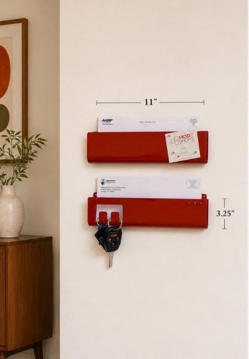 May include: Two red metal wall-mounted mail organizers with a glossy finish. Each unit measures 11 inches wide and 3.25 inches tall. The top organizer holds mail and a small card. The bottom organizer holds mail and features hooks for keys.