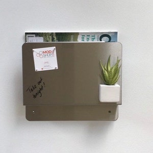 May include: A metallic gray magnetic memo board with a small white square planter holding a green succulent. A magazine rests on top. A small white paper with the text "MOD SHOP" is attached. Handwritten text on the board says "Take out tonight!"