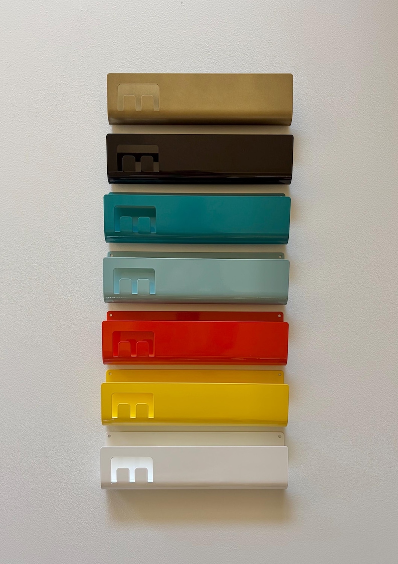 May include: A vertical stack of seven rectangular metal wall-mounted organizers in various colors including gold, black, teal, light blue, red, yellow, and white. Each organizer features a cutout letter E on the left side and a wide open pocket.